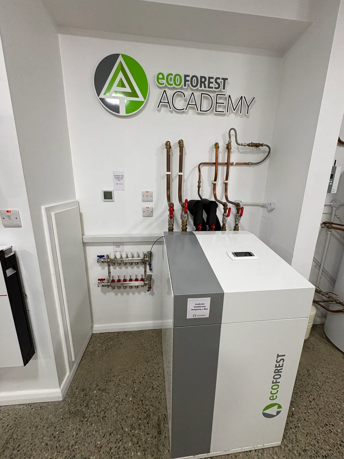 Ecoforest geothermal heat pump unit and heating manifold under the Ecoforest Academy sign in the Efficient Renewables showroom
